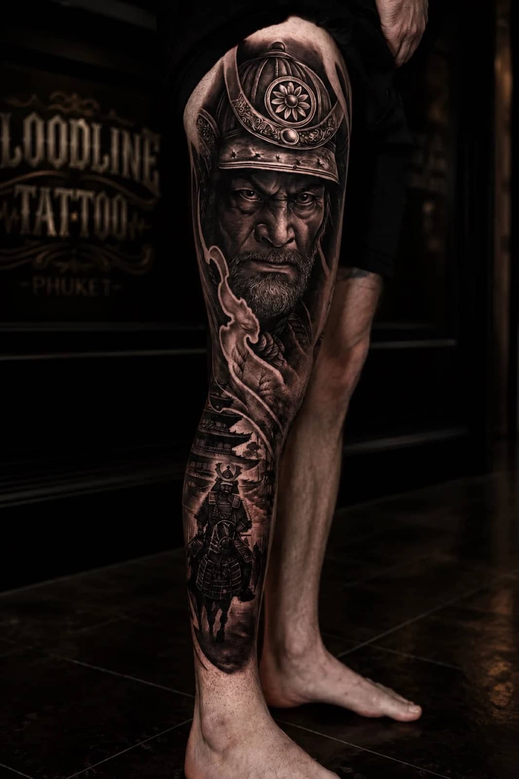 Japanese black and grey leg tattoo with samurai kabuto portrait and mounted samurai scene at Bloodline Tattoo Bali