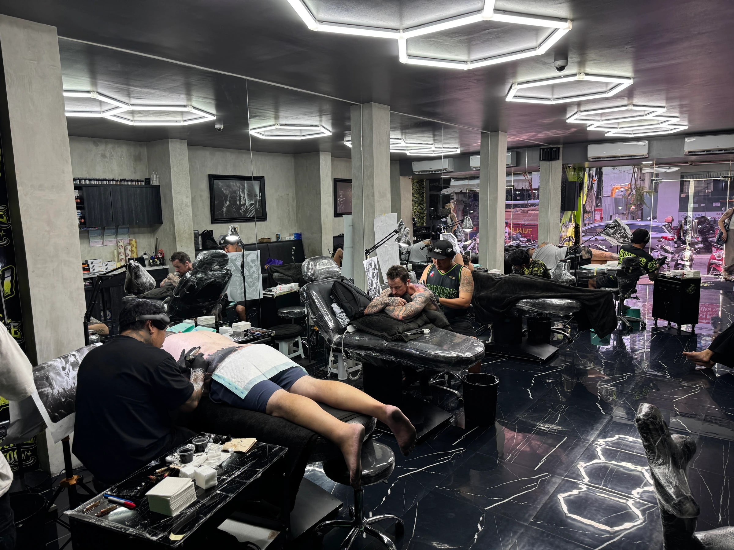 Appointment-only Bloodline Tattoo Bali studio with plastic-wrapped beds, hexagonal lighting, and artists in session