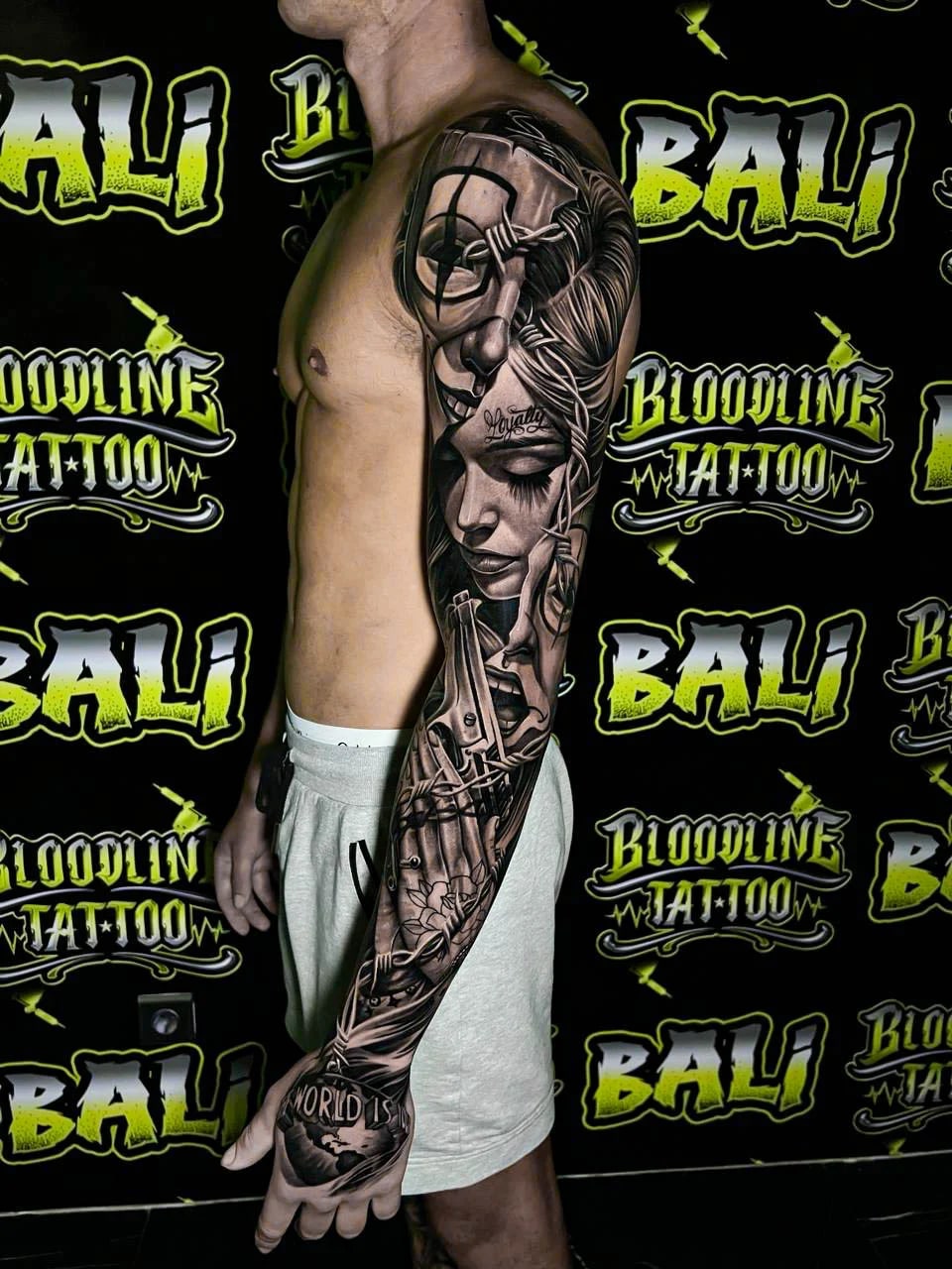 Detailed black and grey Chicano full arm sleeve tattoo featuring a woman portrait, barbed wire, scissors, spiderweb elements, and script at Bloodline Tattoo Bali.