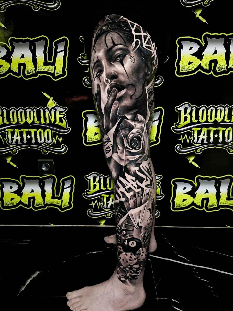 Detailed black and grey Chicano leg sleeve tattoo of a smoking woman with a rose, cards, dice, an 8-ball, and casino chips at Bloodline Tattoo Bali.