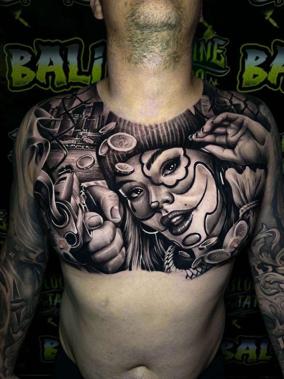Detailed black and grey Chicano chest tattoo featuring a payasa woman, handgun, poker chips, city scene, and rolling coins at Bloodline Tattoo Bali.