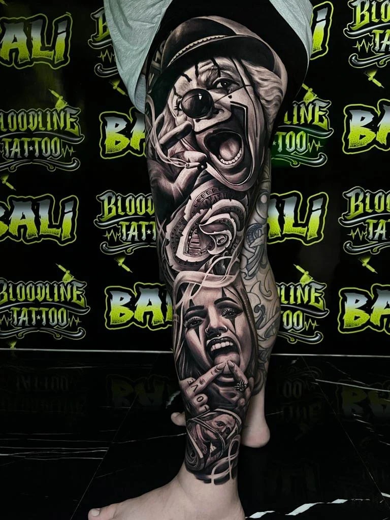 Detailed black and grey Chicano leg sleeve tattoo with a shouting clown, crying woman portrait, swirling script forms, and a lower face detail at Bloodline Tattoo Bali.