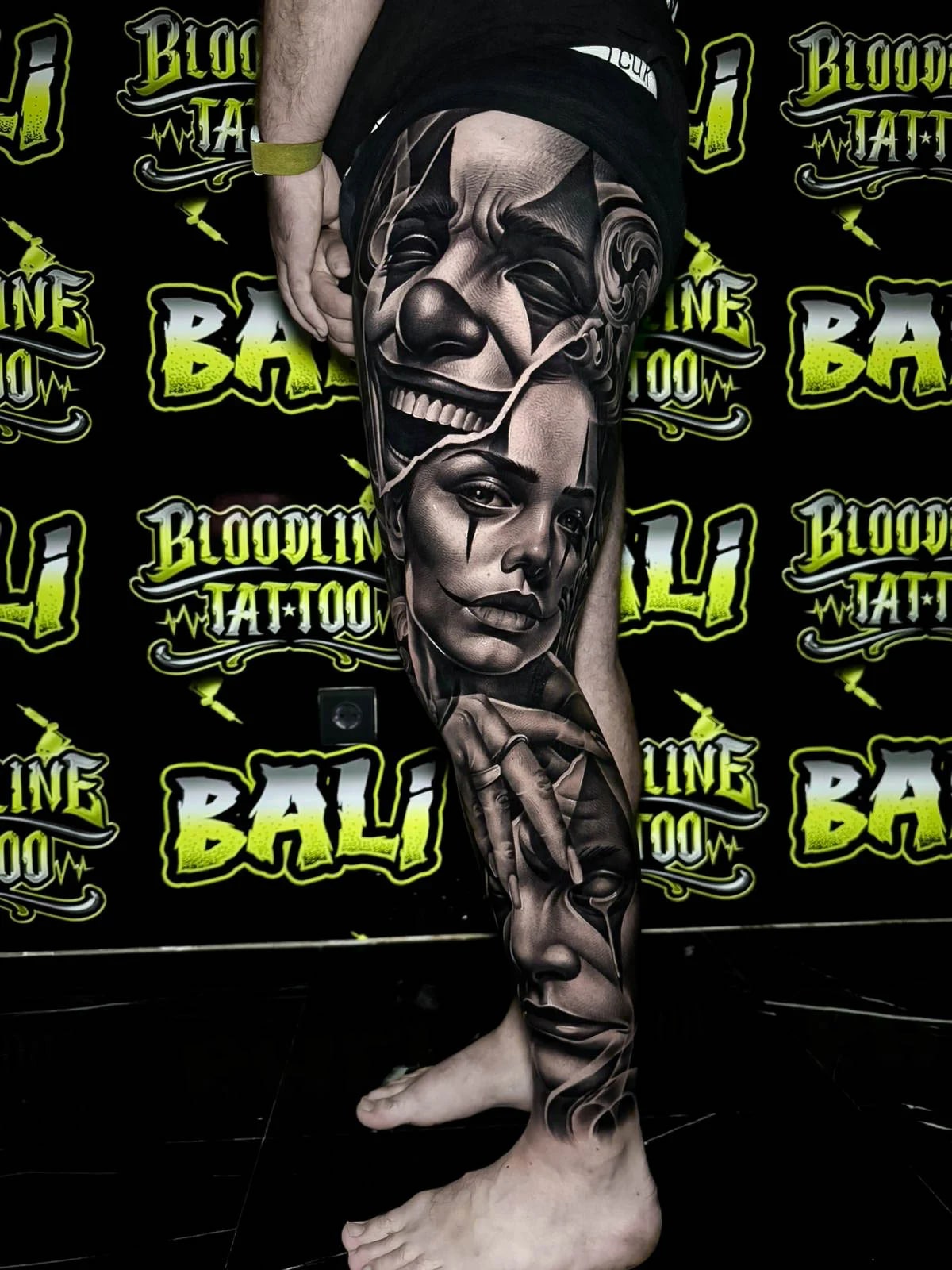Detailed black and grey Chicano leg sleeve tattoo with a split clown face, melancholic female portrait, and layered face studies at Bloodline Tattoo Bali.