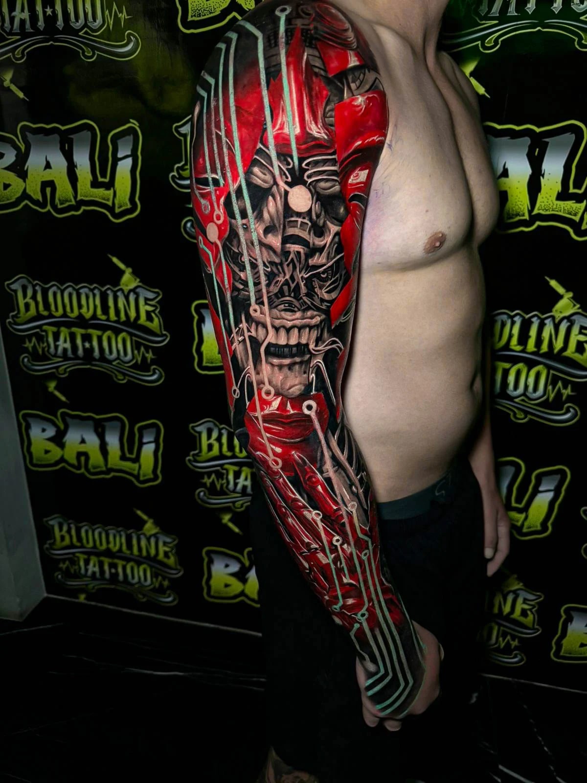 Colour biomechanical full arm sleeve tattoo featuring a snarling skull, red armor panels, and pale circuit linework at Bloodline Tattoo Bali.