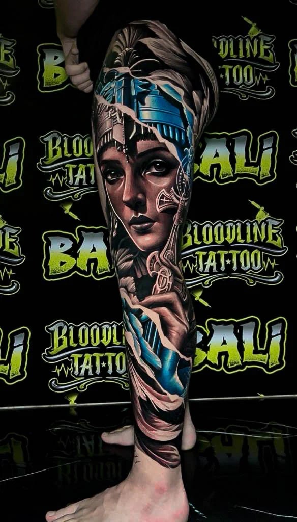 Colour surreal female portrait leg sleeve tattoo with icy blue headpiece details and ornamental filigree flowing through the design at Bloodline Tattoo Bali.