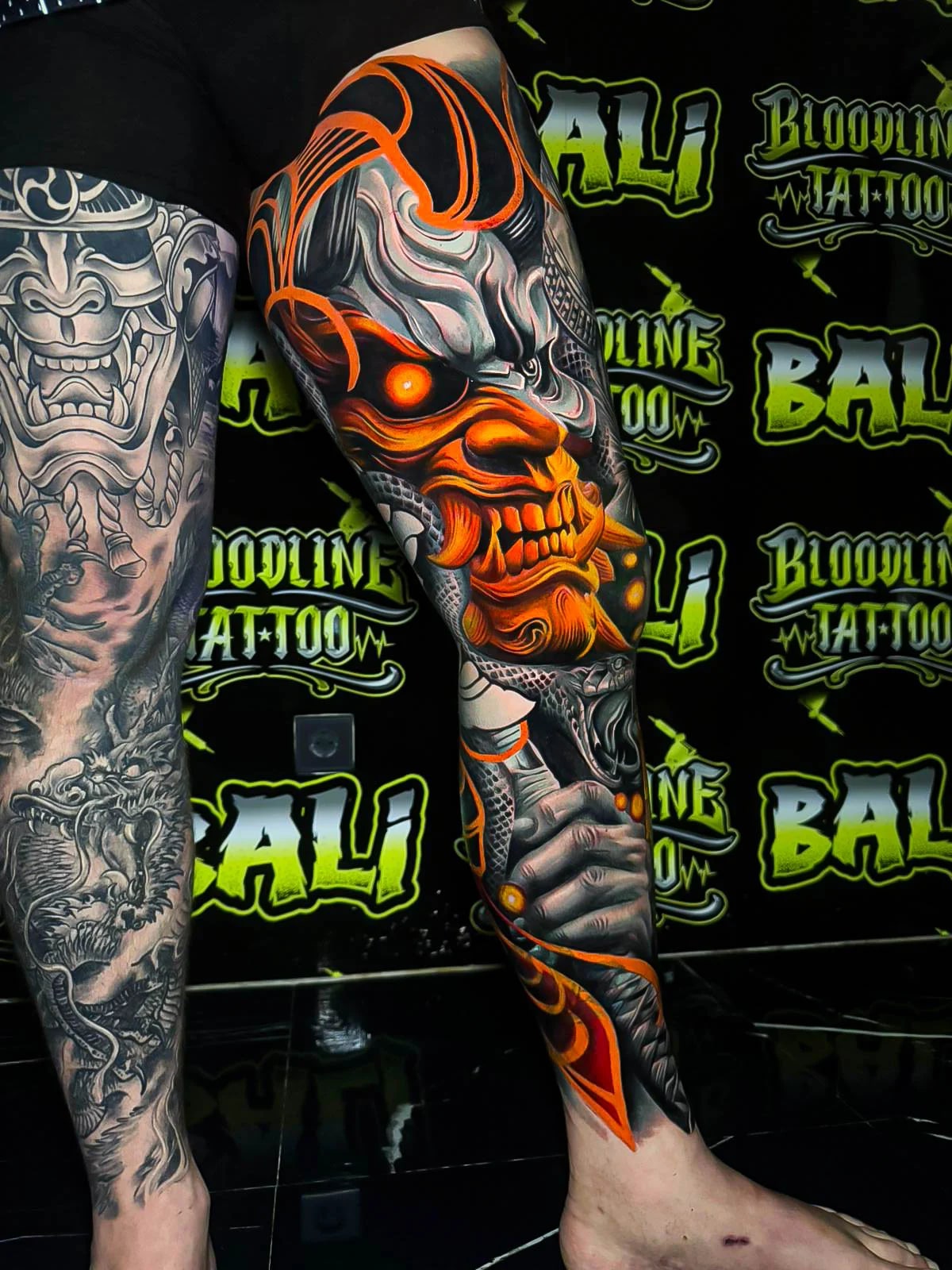 Colour leg sleeve tattoo of a glowing orange oni mask with smoky grey shading, serpent textures, and ember-like highlights at Bloodline Tattoo Bali.