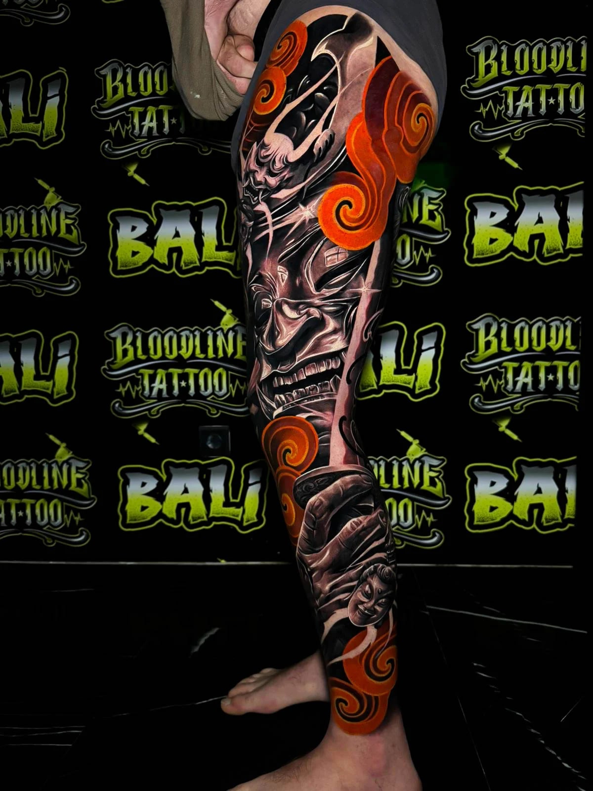 Colour Japanese leg sleeve tattoo featuring a snarling hannya face, bold black shading, and bright orange cloud swirls at Bloodline Tattoo Bali.