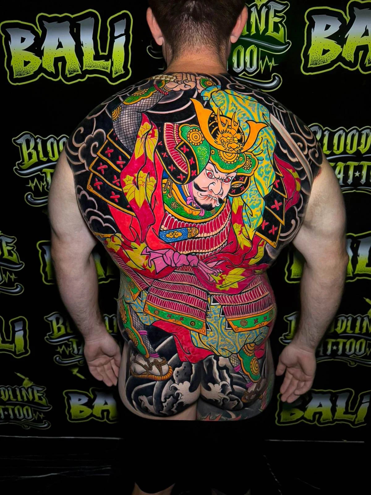 Colour Japanese back piece tattoo of a warrior in ornate armor with red leaves, teal patterns, and crashing waves at Bloodline Tattoo Bali.