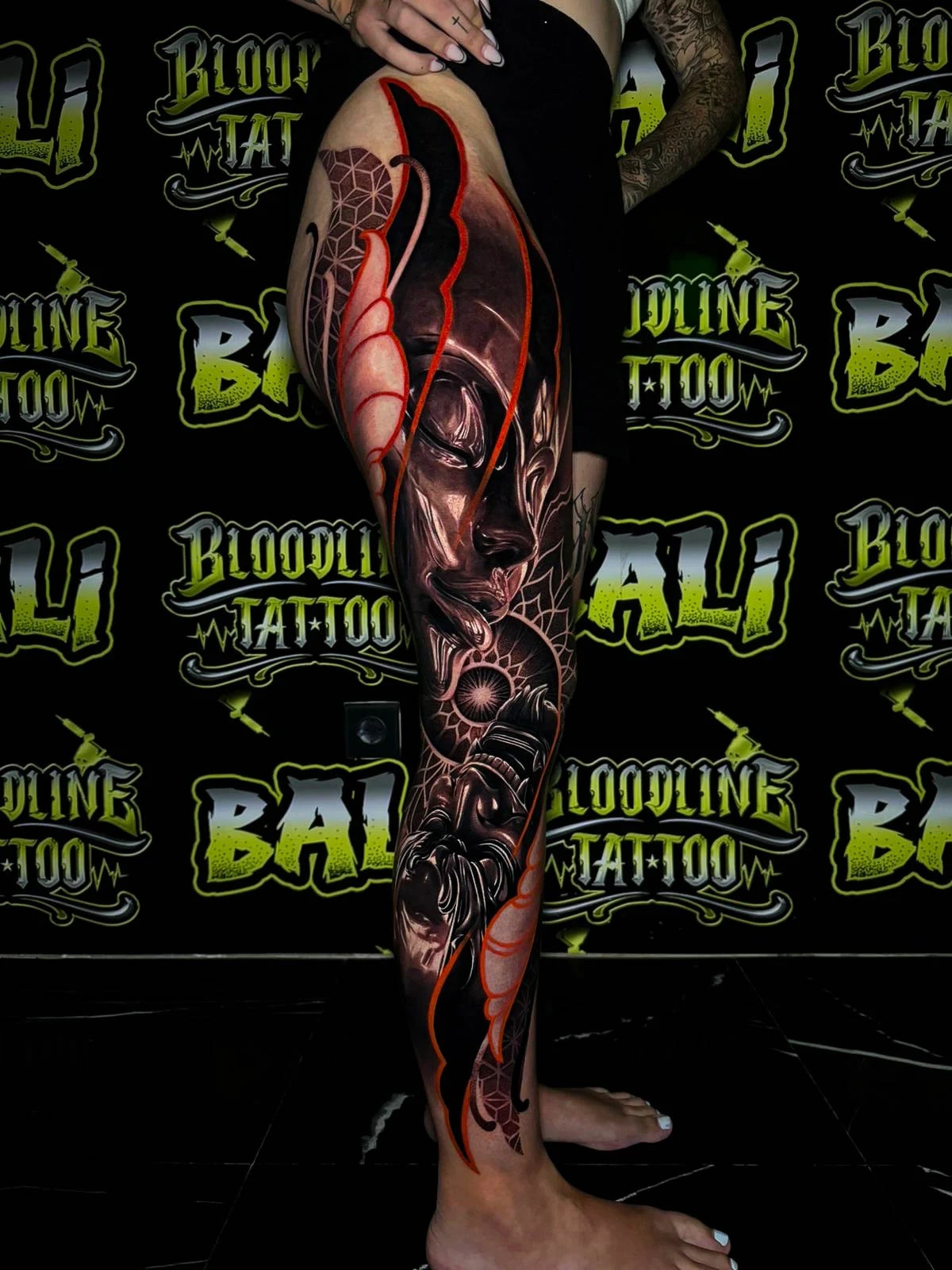 Colour thigh tattoo with a shadowed feminine face, geometric mandala details, and sculpted red-black ornamental framing at Bloodline Tattoo Bali.