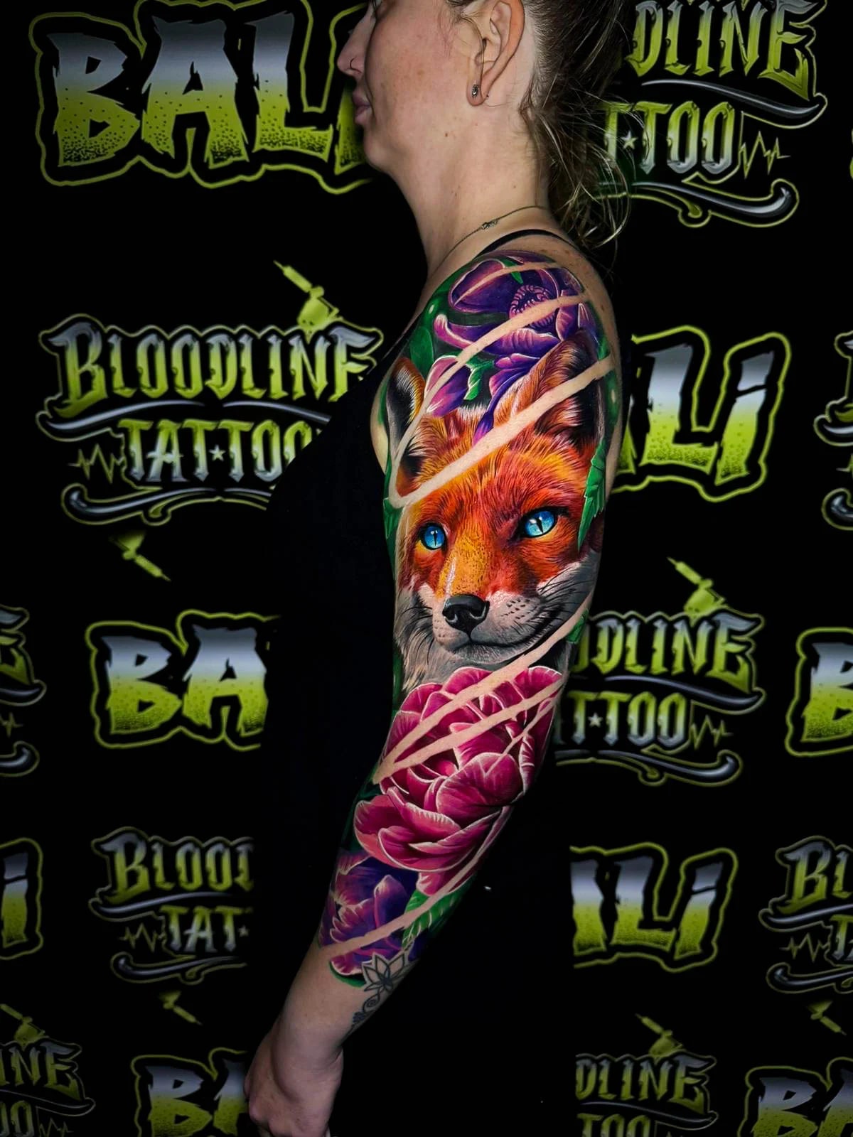 Colour floral arm sleeve tattoo featuring a vivid fox portrait with bright blue eyes, purple blossoms, and pink peonies at Bloodline Tattoo Bali.