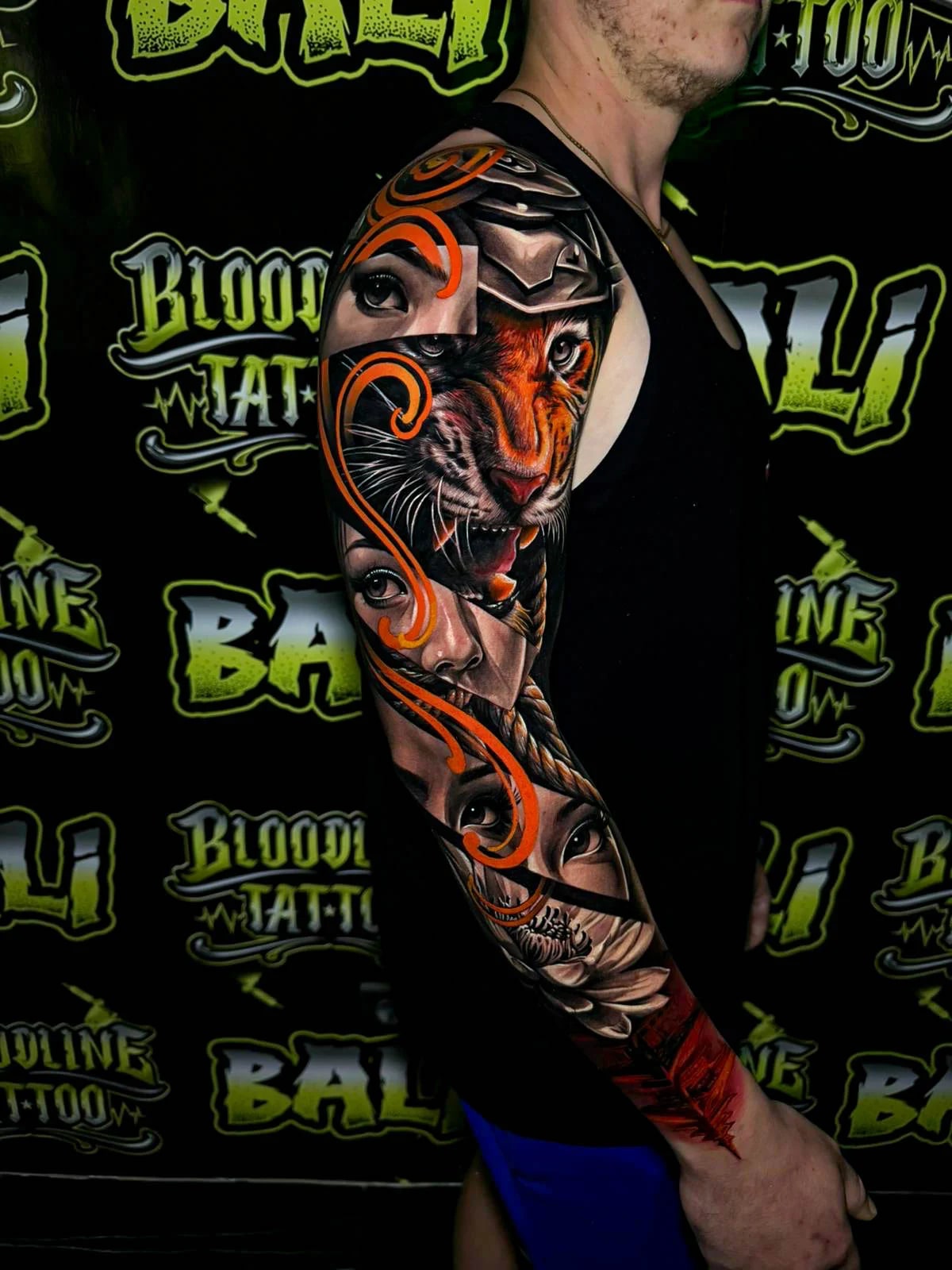 Colour full arm sleeve tattoo featuring a roaring tiger, multiple female eyes, braided hair, and orange filigree accents at Bloodline Tattoo Bali.