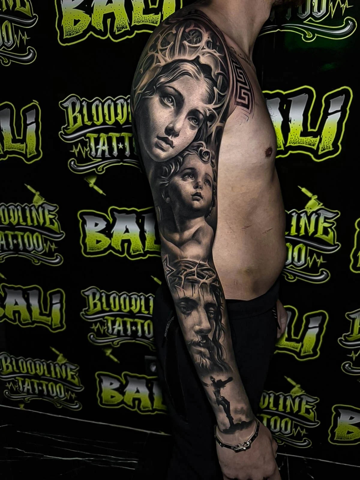 Healed black-and-grey sleeve with Madonna, cherub, and Christ portraiture, showing soft portrait realism and stable healed line integrity at Bloodline Tattoo Bali.