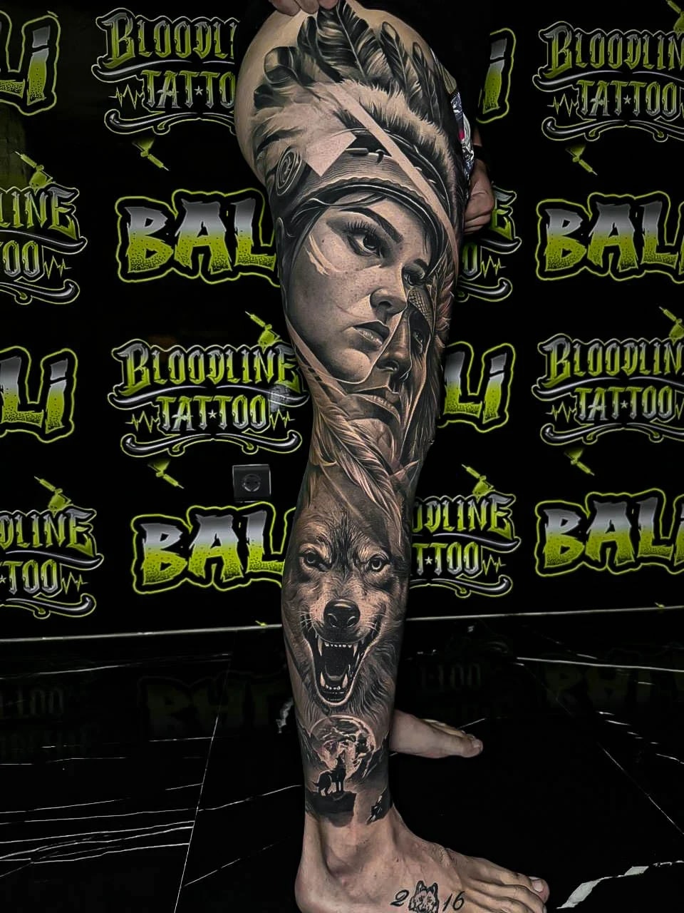 Healed realism leg sleeve with a Native portrait, feathers, and snarling wolf, showing smooth grey transitions and durable healed contrast at Bloodline Tattoo Bali.