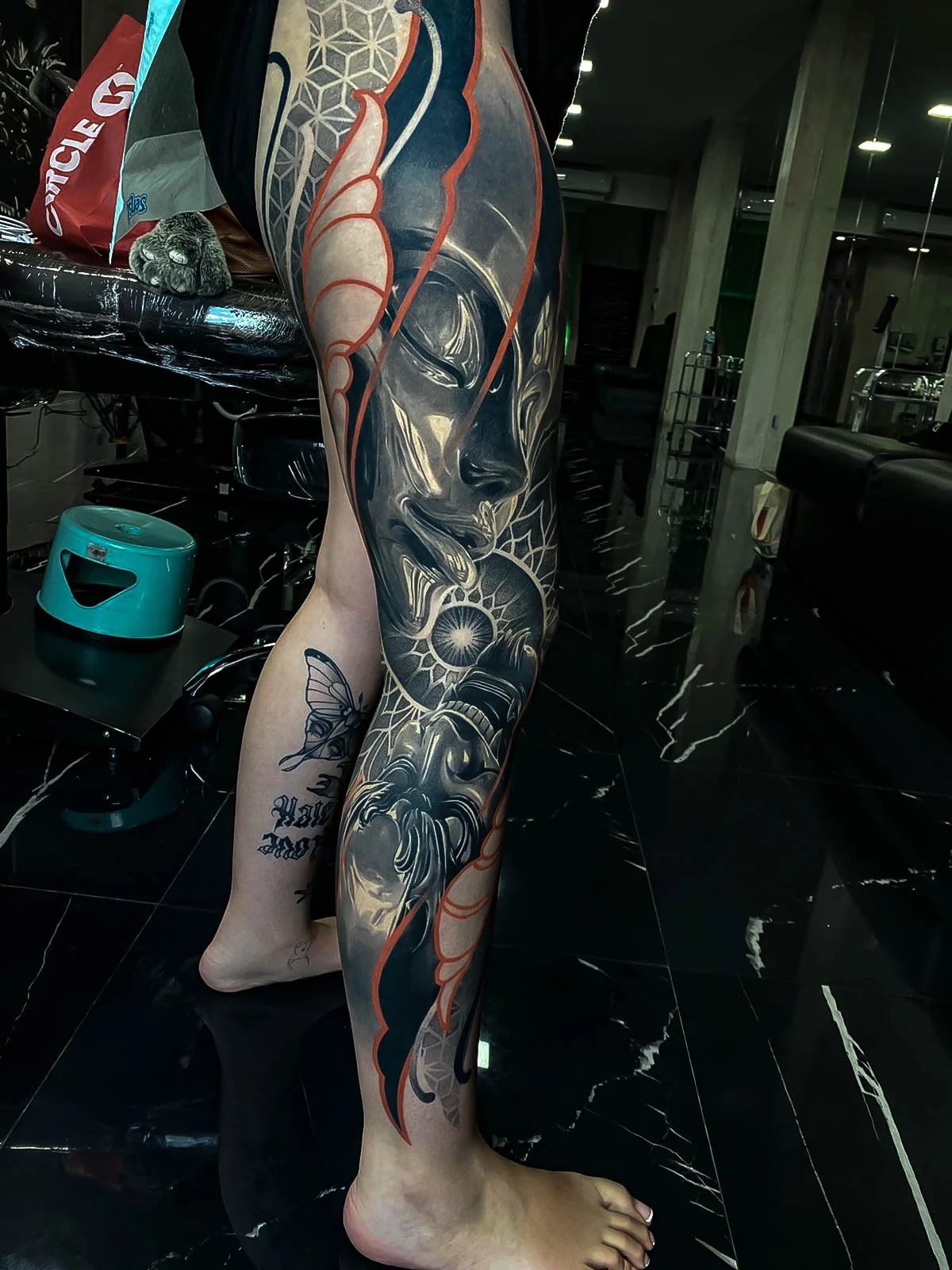 Healed leg sleeve with a female face, butterfly wing, sacred-geometry accents, and red contour highlights, holding smooth healed contrast at Bloodline Tattoo Bali.
