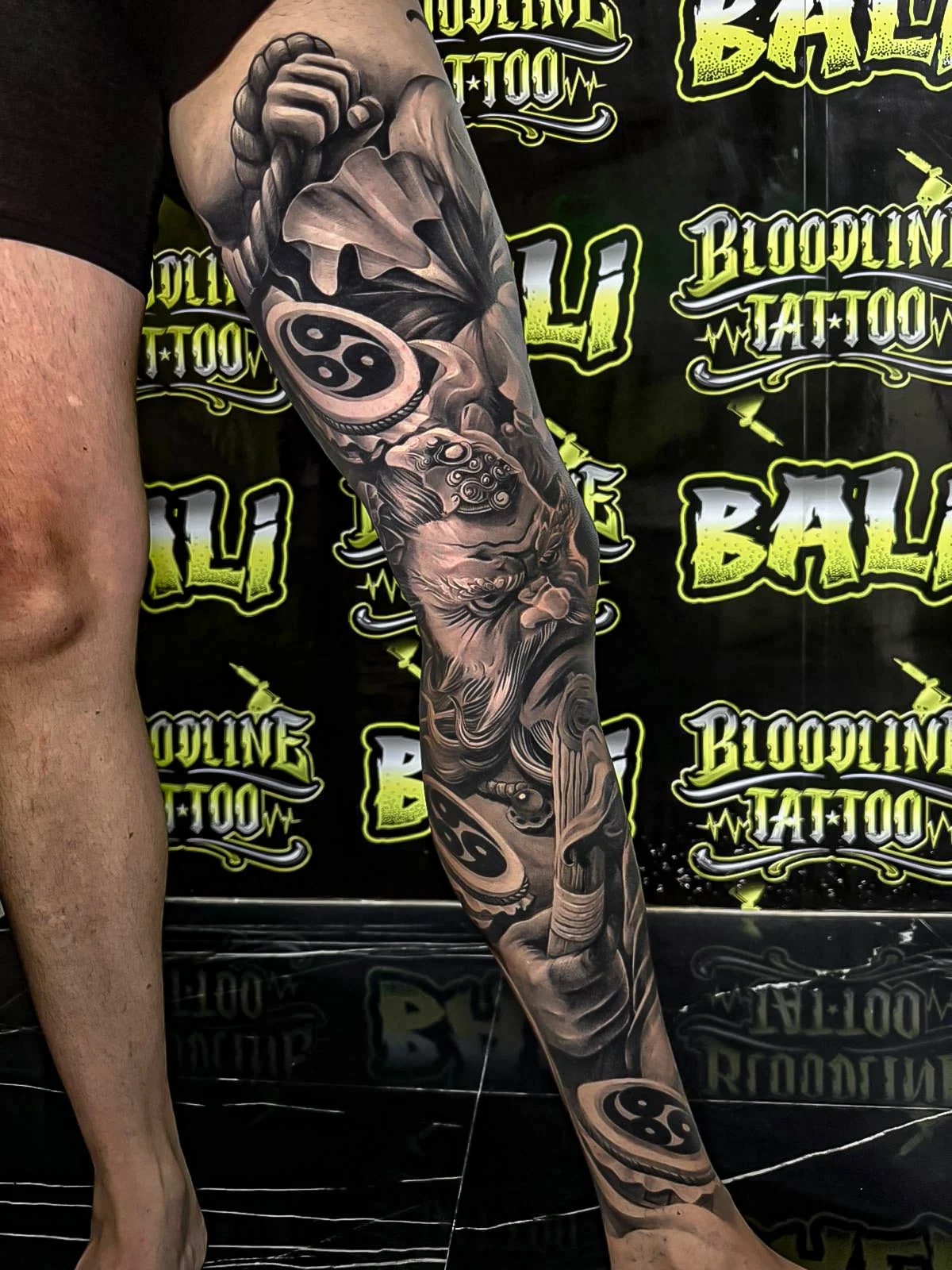 Healed black-and-grey leg sleeve with yin-yang discs, peony petals, and lionlike portrait elements, holding smooth gradients and healed line integrity at Bloodline Tattoo Bali.