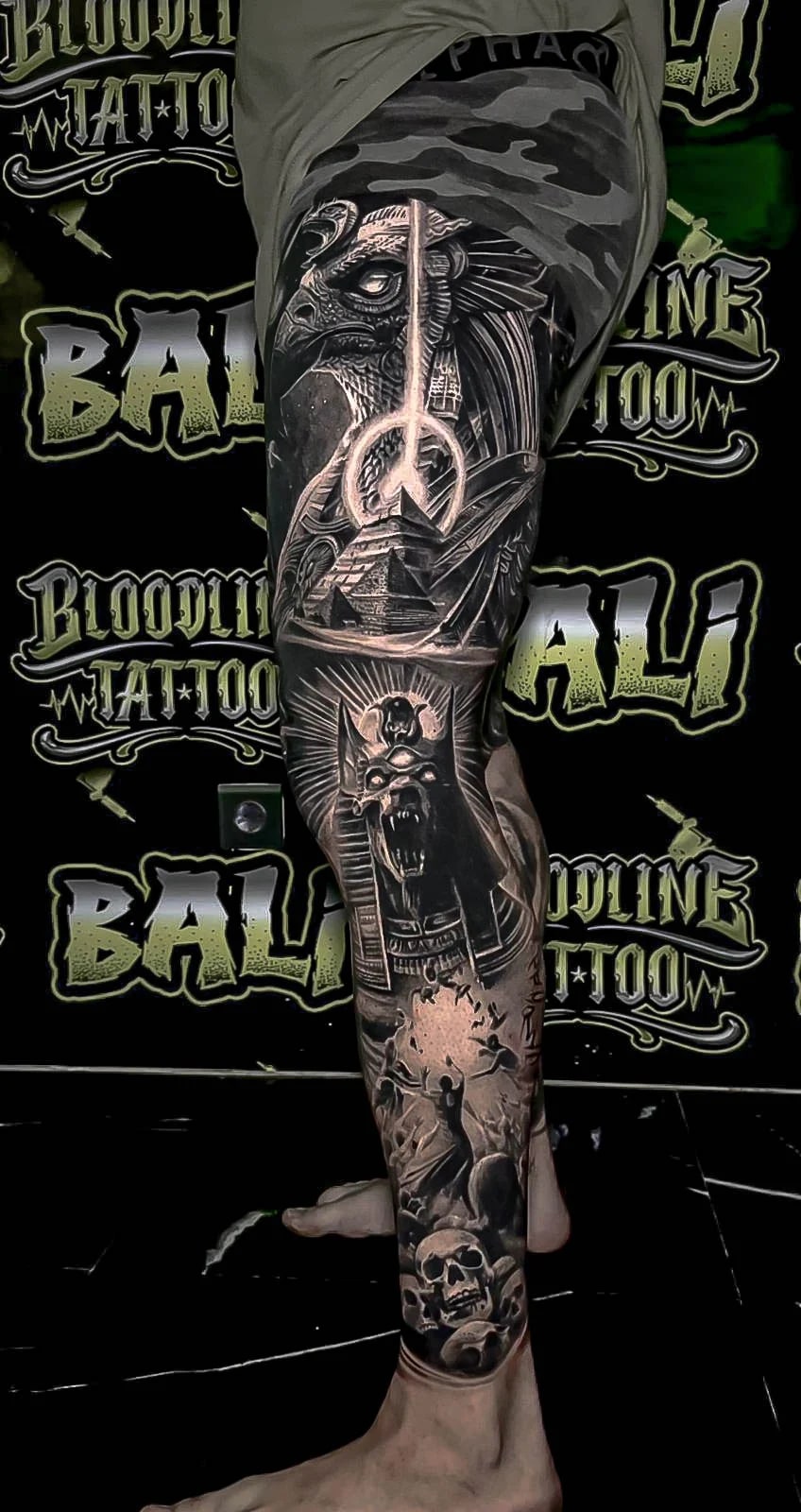 Healed black-and-grey leg sleeve with an eagle head, pyramid, radiant figure, and skulls, showing crisp healed contrast and depth at Bloodline Tattoo Bali.