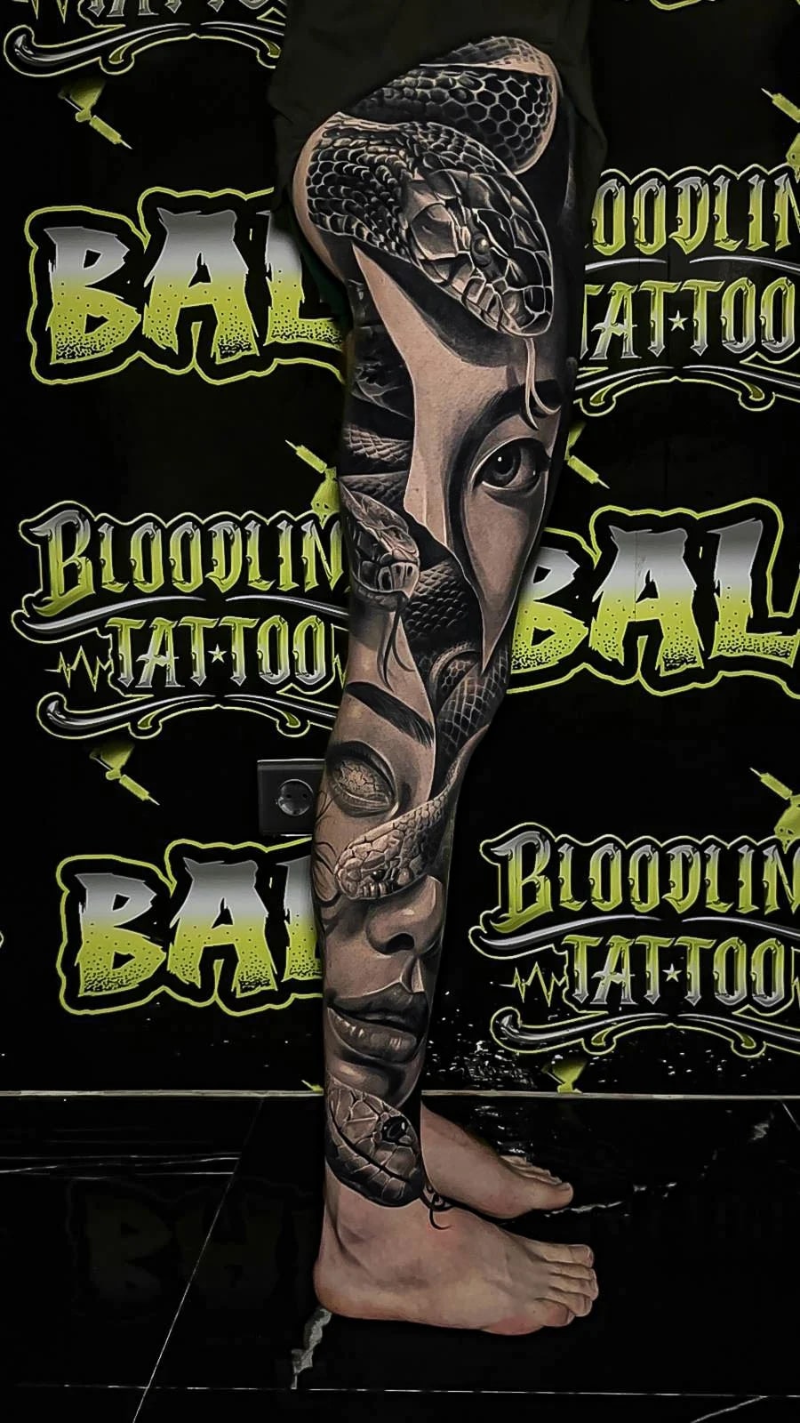 Healed black-and-grey leg sleeve with coiled snakes and female portraits, showing velvety blacks and clean healed facial detail at Bloodline Tattoo Bali.