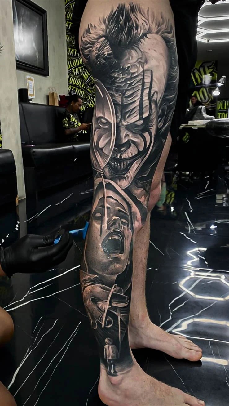 Healed horror leg sleeve with a sinister clown, theatre masks, and screaming face imagery, showing strong blacks and clean healed transitions at Bloodline Tattoo Bali.