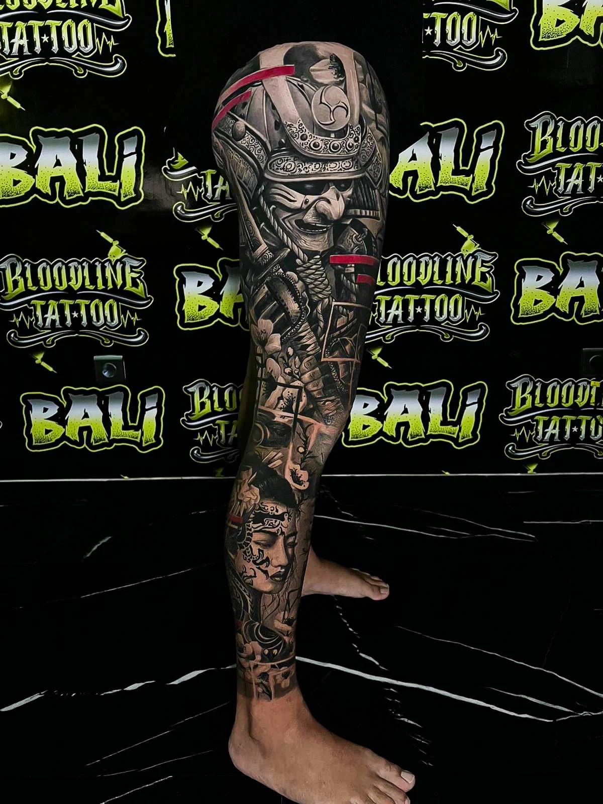 Healed samurai leg sleeve with a kabuto helmet, warrior face, and red accent slashes, keeping bold blacks and clean healed edges at Bloodline Tattoo Bali.