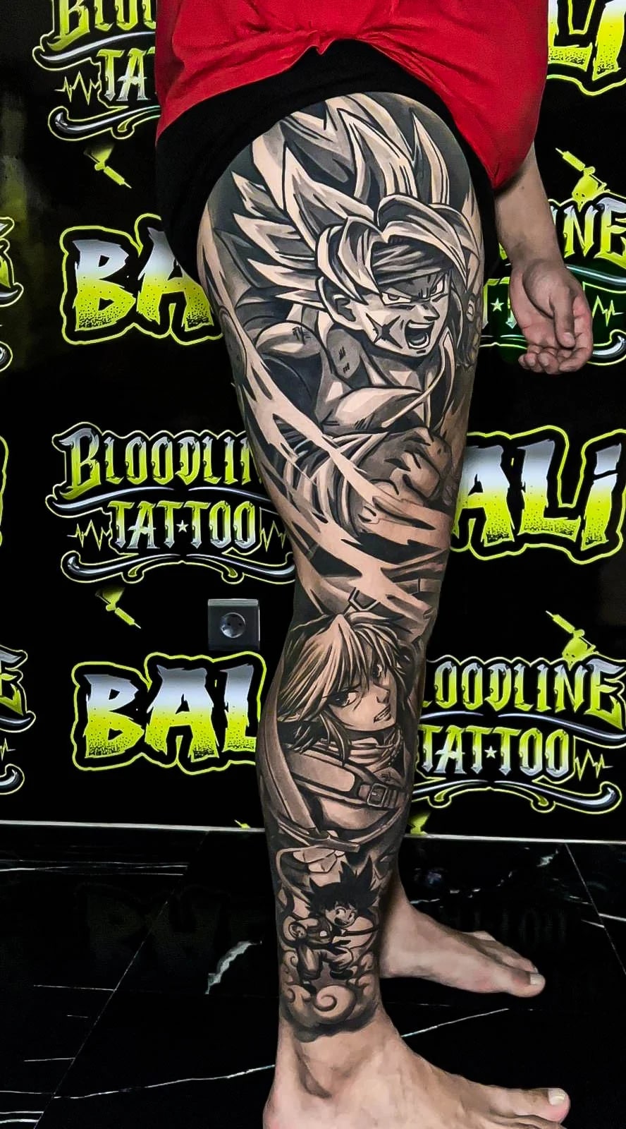 Healed anime leg sleeve with spiky-haired hero portraiture and manga panels, showing smooth black-and-grey saturation and crisp healed contours at Bloodline Tattoo Bali.