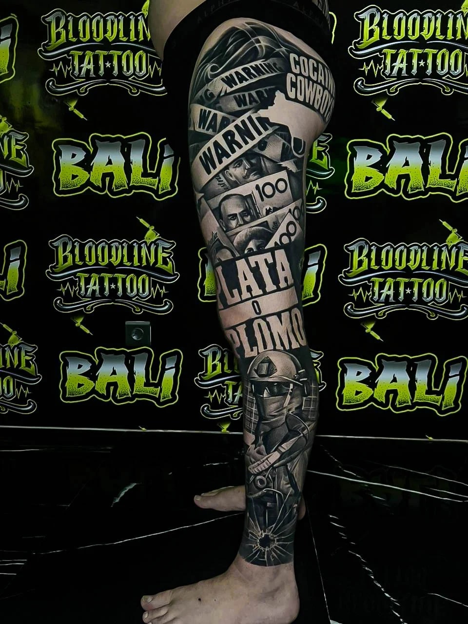 Healed collage leg sleeve with money, bold lettering, warning tape, and biker imagery, showing strong healed contrast and sharp edge definition at Bloodline Tattoo Bali.
