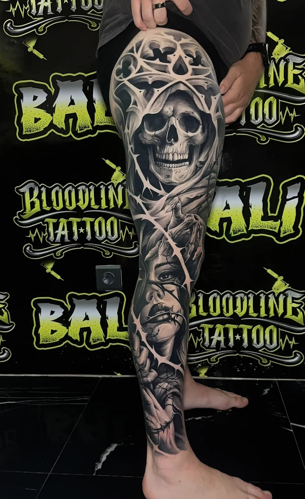 Healed leg sleeve with a hooded skull, stitched female face, and barbed wire framing, holding bold blacks and crisp healed contrast at Bloodline Tattoo Bali.