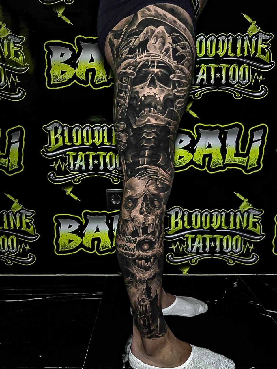 Healed black-and-grey leg sleeve with a screaming skull, skeletal hands, and revolver details, keeping bold blacks and crisp healed detail at Bloodline Tattoo Bali.