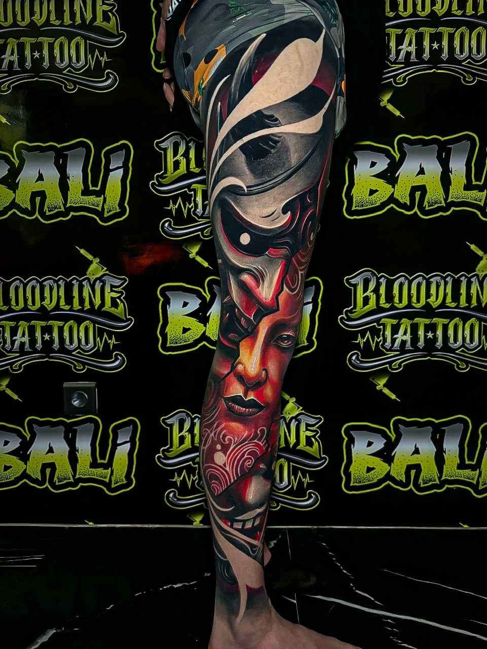 Healed neo-surreal leg sleeve with split mask shapes, red facial tones, and flowing black forms, holding smooth healed saturation at Bloodline Tattoo Bali.