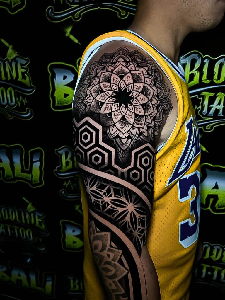 Shoulder blackwork sleeve with a lotus mandala cap, hexagon bands, and radiating geometric flowerwork in dense dot shading at Bloodline Tattoo Bali.