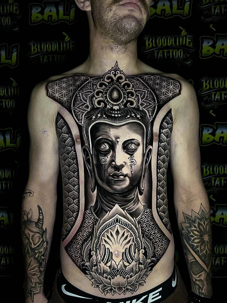 Full torso Buddha composition with Flower of Life shoulders, ornamental crown work, and dot-shaded sacred geometry framed down the sternum at Bloodline Tattoo Bali.