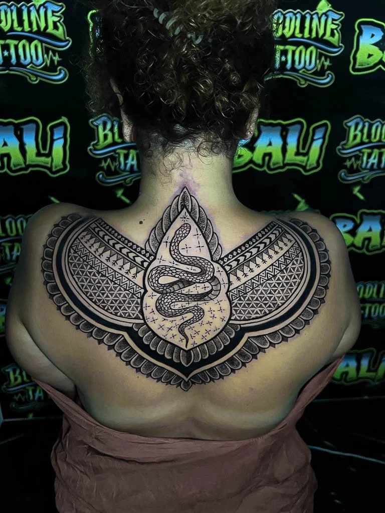 Upper-back blackwork with a coiled snake centerpiece, winged ornamental panels, and dense geometric patterning across both shoulders at Bloodline Tattoo Bali.