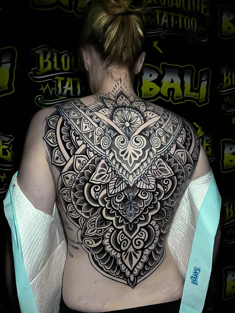 Symmetrical ornamental backpiece with compass-lotus detailing, layered petals, and soft dotwork shading tapering toward the lower back at Bloodline Tattoo Bali.