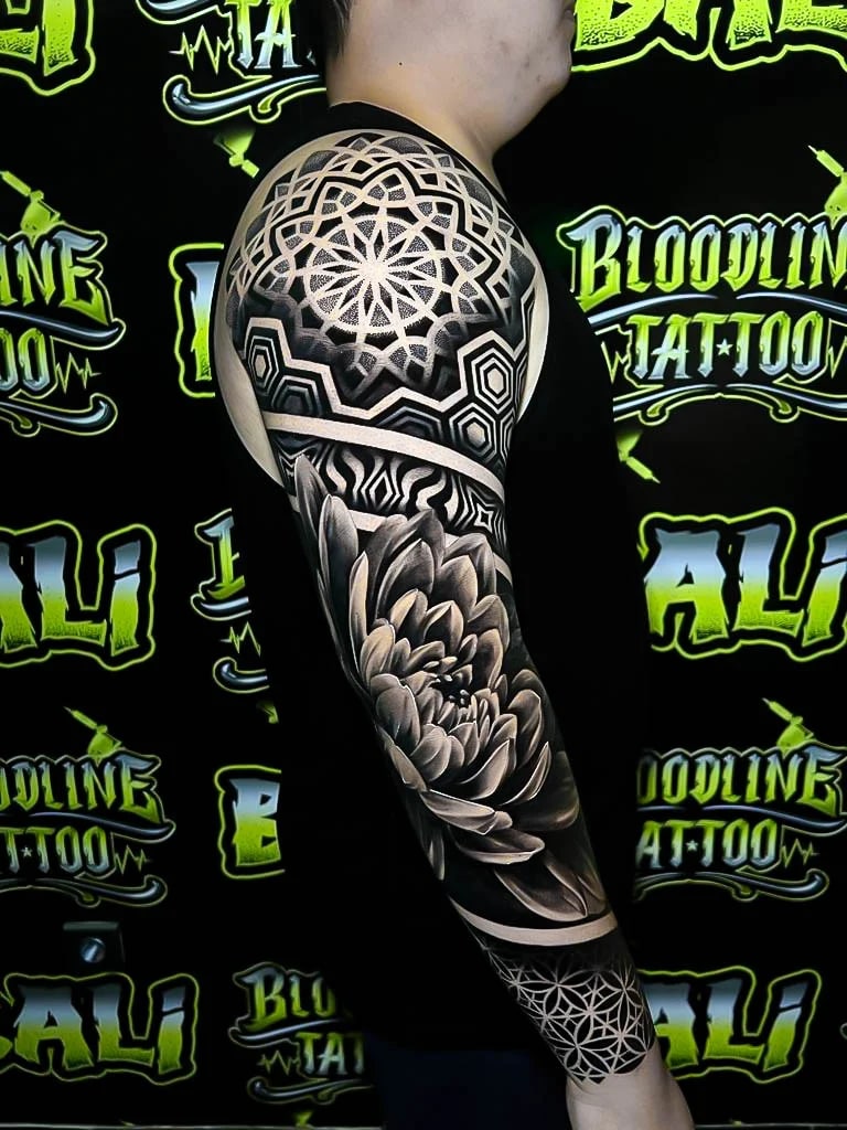 Sleeve with a shoulder mandala cap, black-and-grey peony shading, and a Flower of Life wrist panel balanced by bold negative space at Bloodline Tattoo Bali.