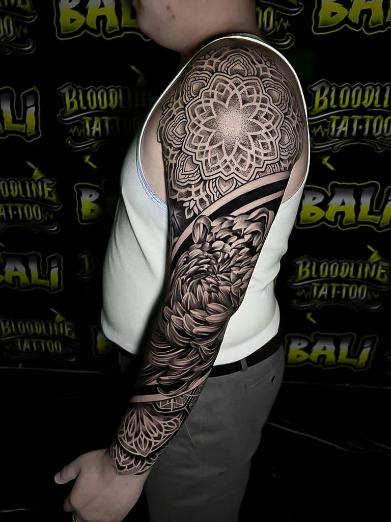 Upper-arm mandala cap with layered petals, a black-and-grey chrysanthemum, and ornamental wrist geometry finished in smooth dot shading at Bloodline Tattoo Bali.