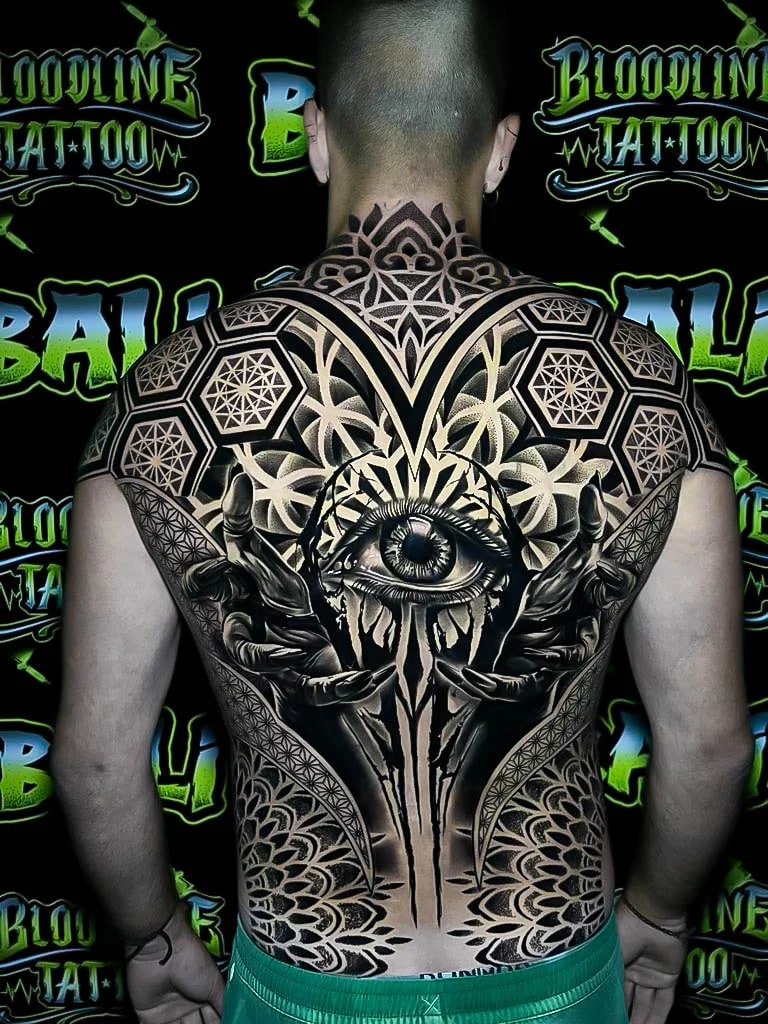 Full-back sacred geometry piece with an all-seeing eye, mirrored hands, hexagon fields, and petaled blackwork framing the spine at Bloodline Tattoo Bali.