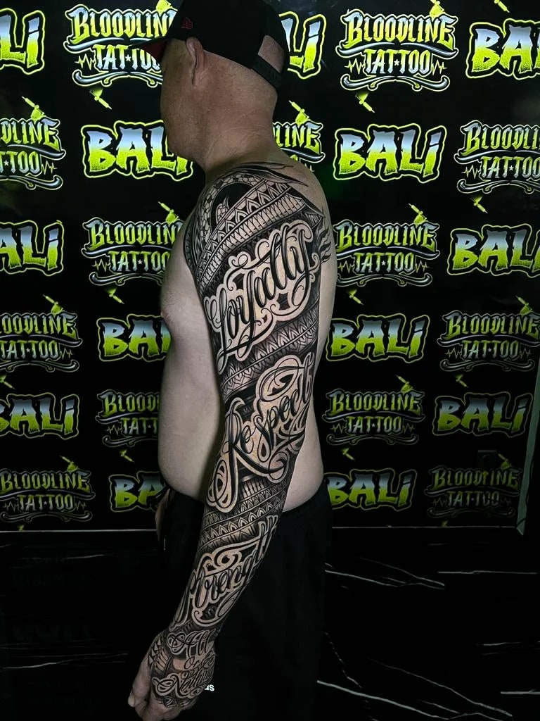 Polynesian-style script sleeve with ornamental tribal bands, interlocking triangle motifs, and smooth blackwork tapering down the forearm at Bloodline Tattoo Bali.