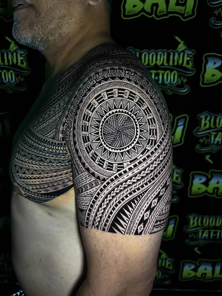 Polynesian chest and shoulder work with a sun-disc roundel, woven linework, and tightly packed tribal bands rendered in crisp blackwork at Bloodline Tattoo Bali.