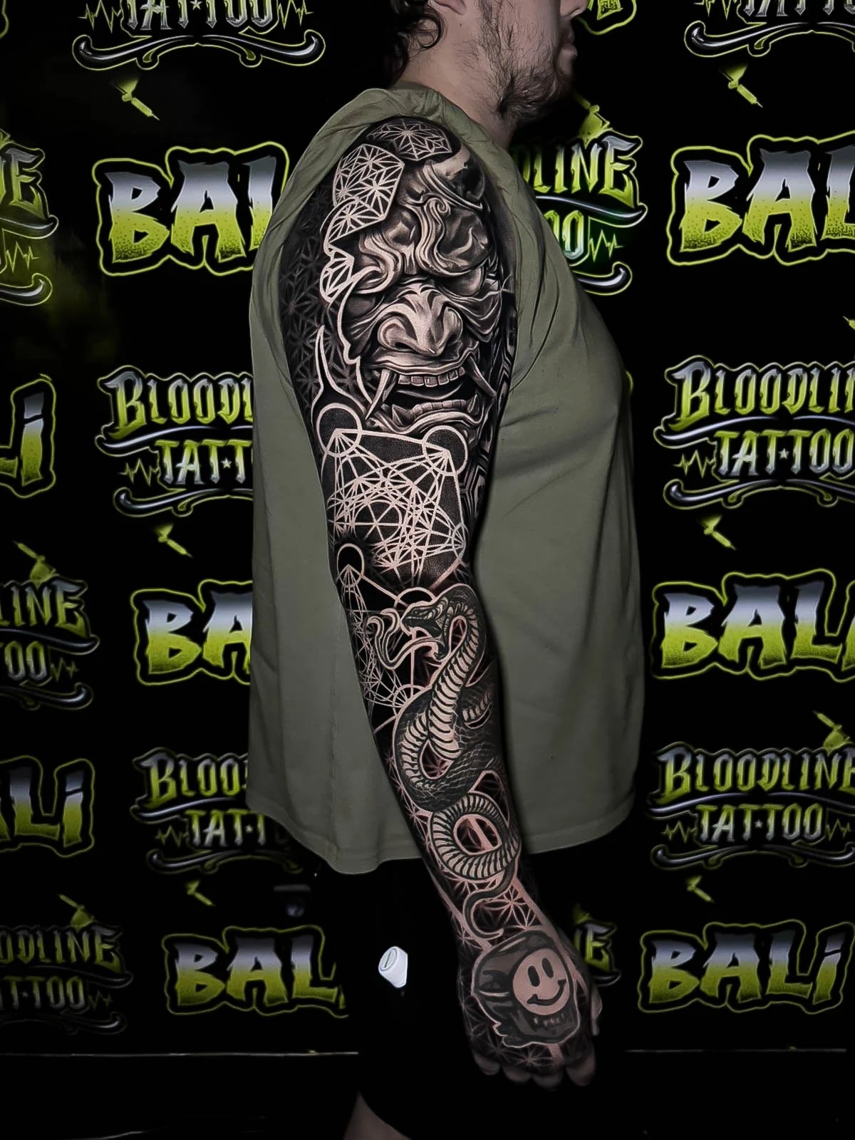 Black-and-grey sleeve with a Hannya mask, serpent details, Metatron-style geometry, and dense dotwork contrast from shoulder to hand at Bloodline Tattoo Bali.
