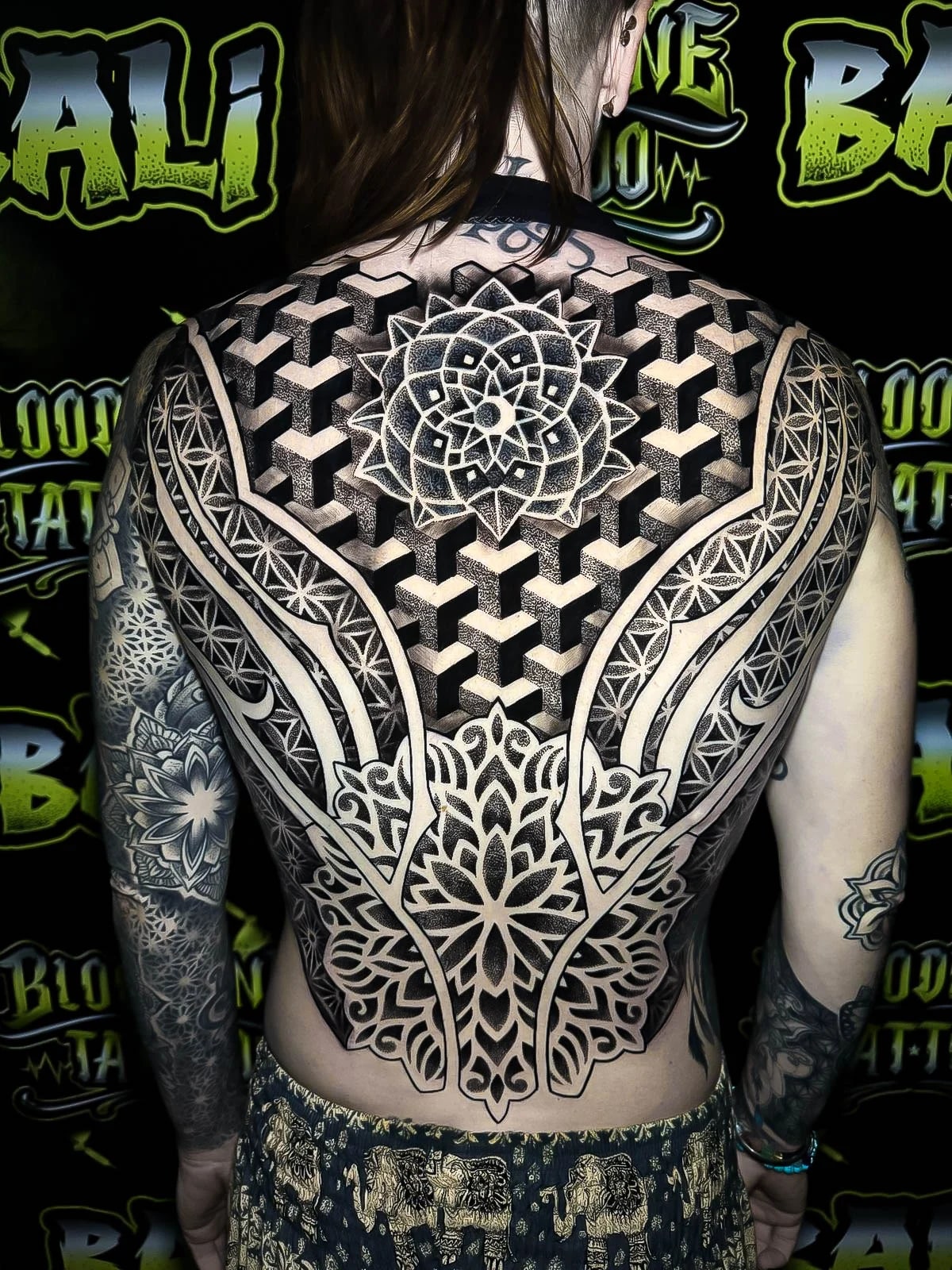 Full-back geometric piece with a central lotus mandala, 3D cube tessellation, and Flower of Life borders sweeping over both shoulders at Bloodline Tattoo Bali.