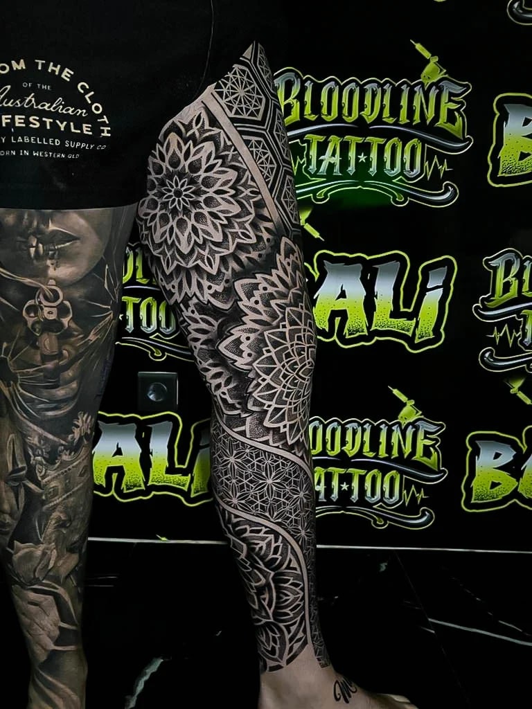 Side leg mandala sleeve with layered floral rosettes, dotwork shading, and geometric lower-leg panels balanced by clean blackout bands at Bloodline Tattoo Bali.
