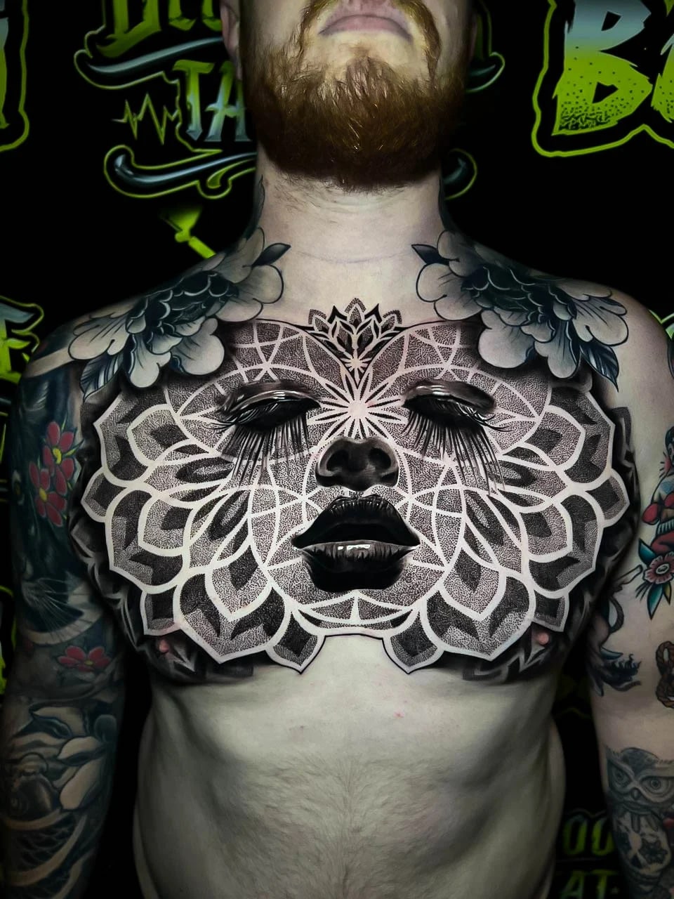 Chest blackwork with a woman's face set inside a wide lotus mandala, heavy stippled shading, and petaled geometry spanning pec to pec at Bloodline Tattoo Bali.