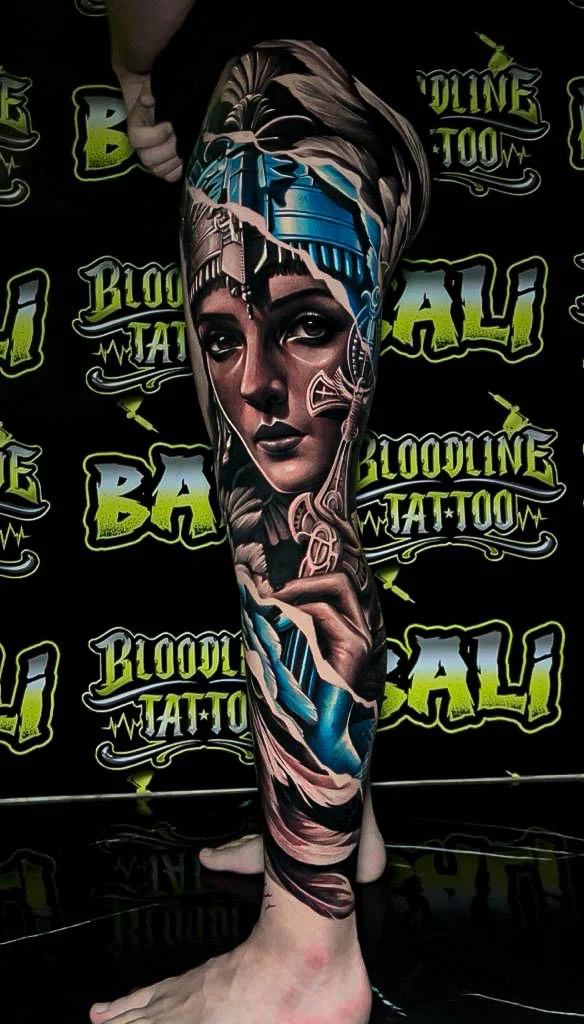 Colour surreal female portrait leg sleeve tattoo with icy blue headpiece details and ornamental filigree flowing through the design at Bloodline Tattoo Bali.