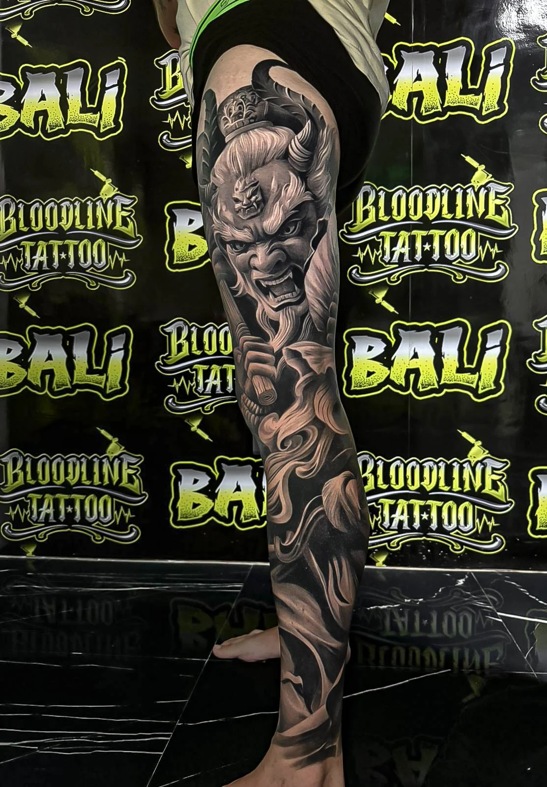 Healed black-and-grey leg sleeve with a horned Oni face and smoke-like hair flow, showing velvety shading and sharp healed line integrity at Bloodline Tattoo Bali.