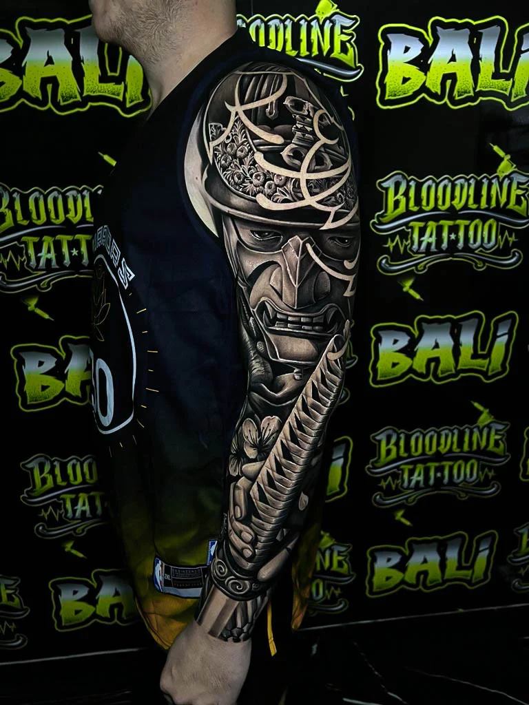 Black and grey Japanese full sleeve with a samurai mask, katana, and cherry blossoms at Bloodline Tattoo Bali.