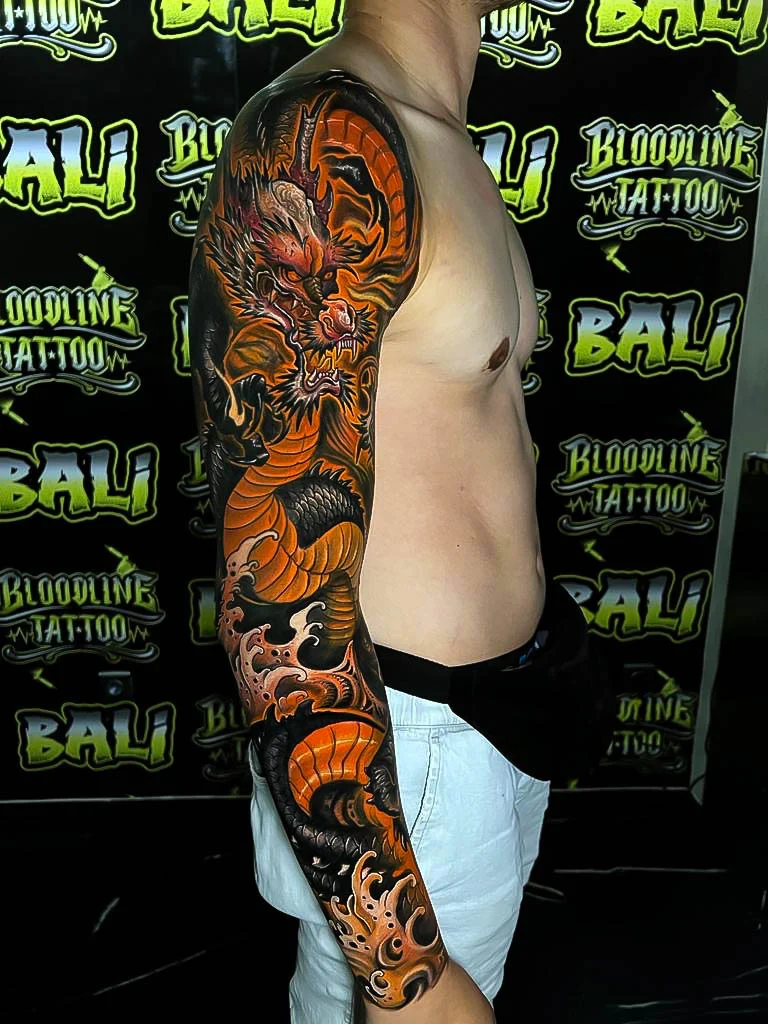 Japanese colour full sleeve with an orange dragon, black background, and crashing waves at Bloodline Tattoo Bali.