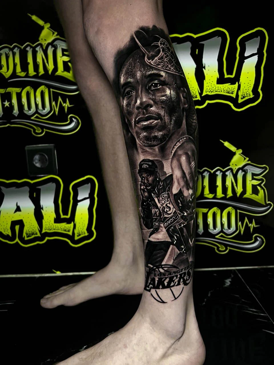 Black and grey portrait realism calf tattoo of Kobe Bryant with Lakers championship imagery and basketball details at Bloodline Tattoo Bali.