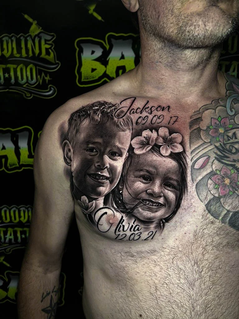 Black and grey portrait realism chest tattoo of two smiling children with floral accents, names, and birth dates at Bloodline Tattoo Bali.