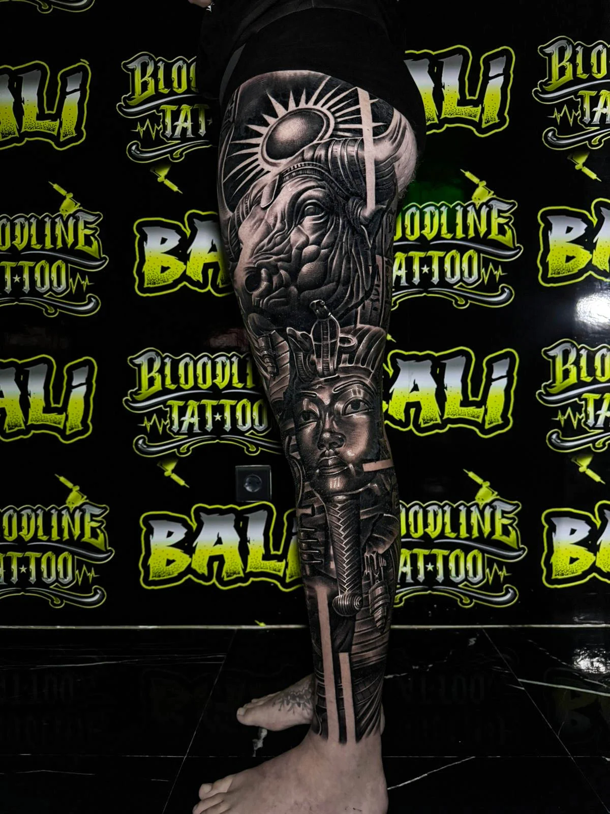A black and grey realism full leg sleeve with a moonlit eye, skull detail, and dark gothic elements stacked along the shin, at Bloodline Tattoo Bali.